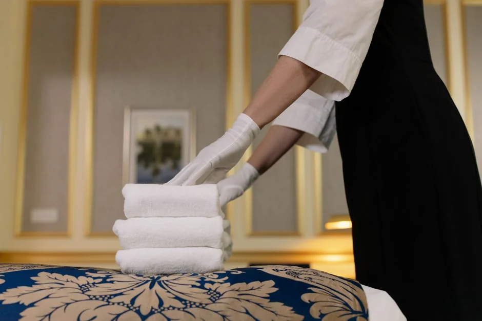 Individual in protective gear cleaning microwave using spray bottle and cloth indoors.